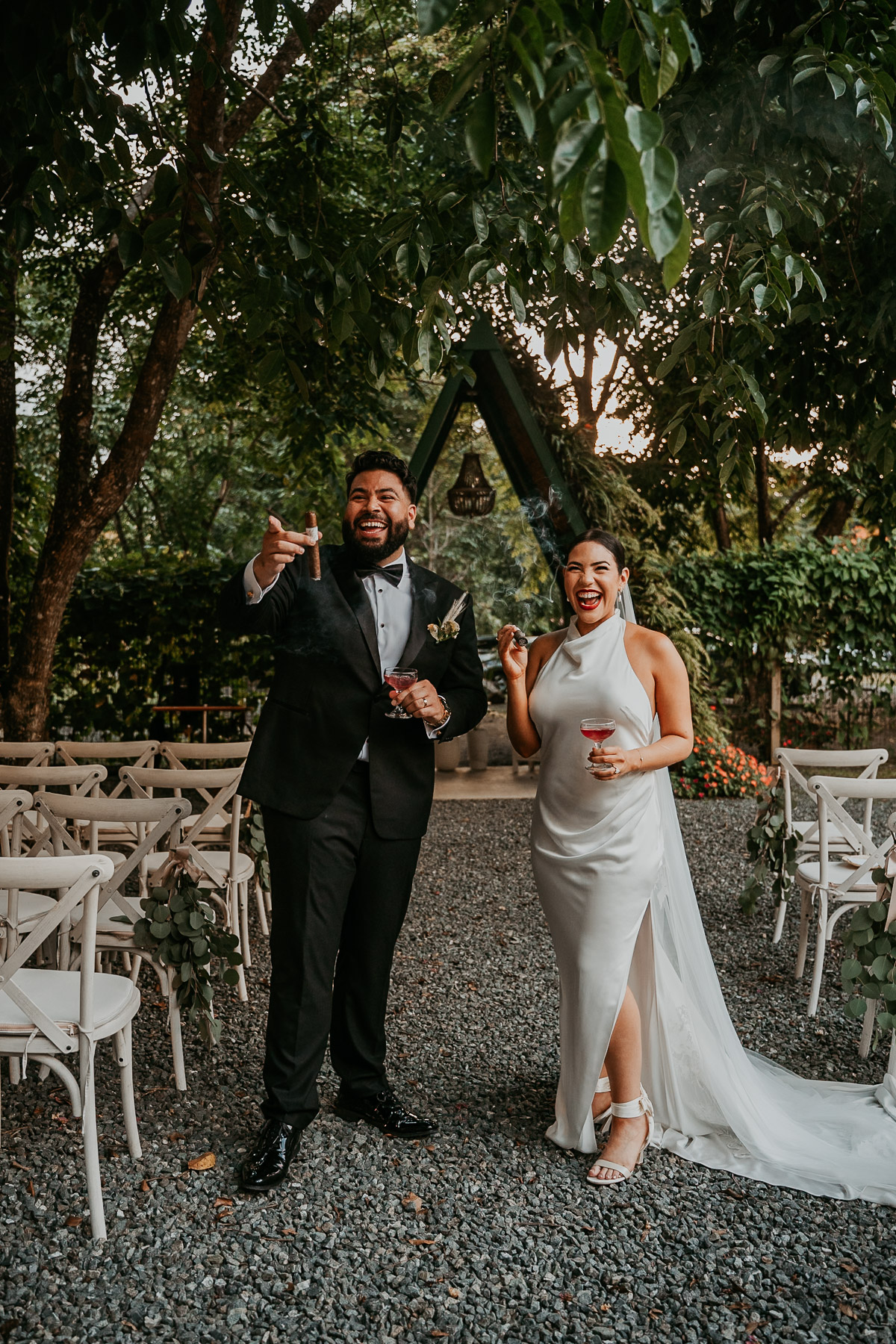 Candid photo of a newlywed couple laughing and smoking artisanal cigars at their alternative mountain wedding.