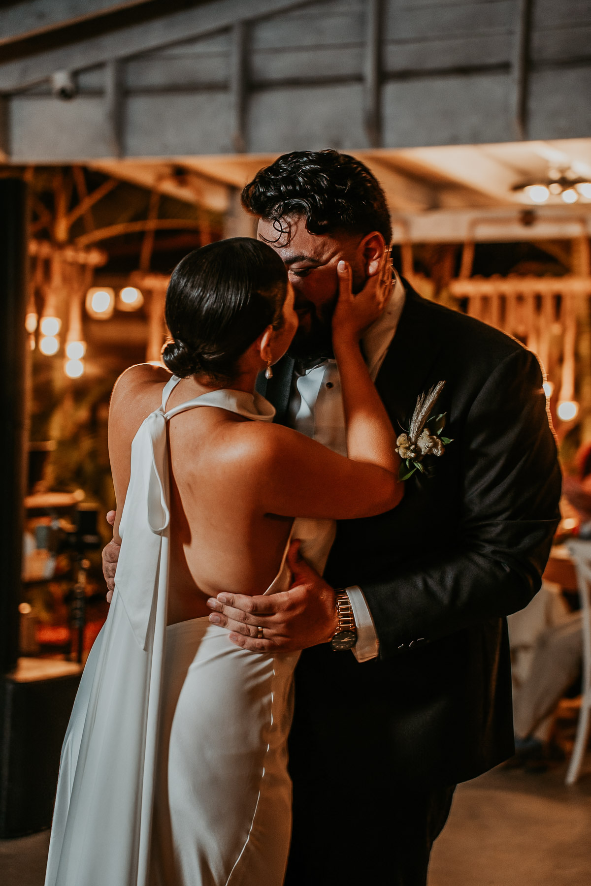 The newlyweds sharing a kiss during their first dance under the vaulted ceilings and ambient lighting of La Bromelia hall.