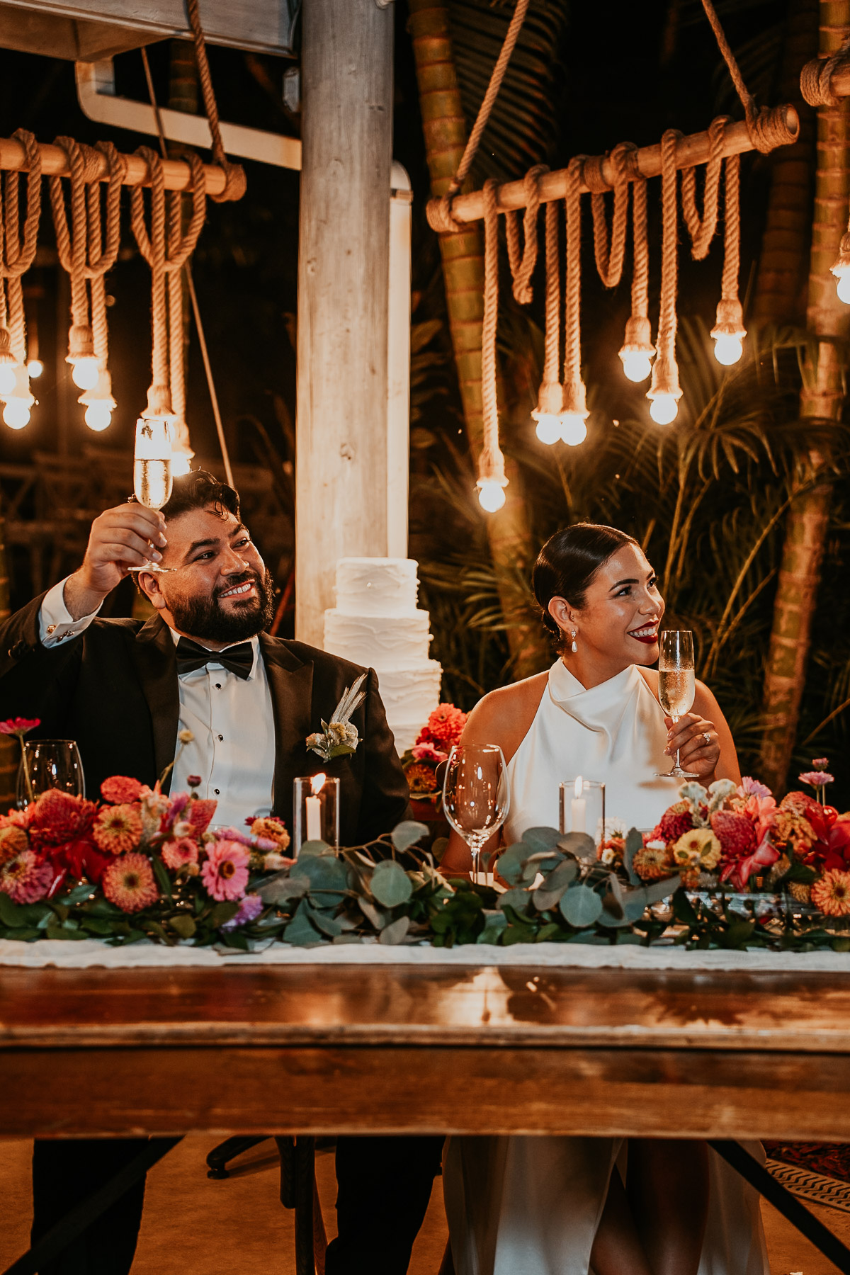 Newlywed couple raising their glasses for a toast surrounded by friends and family.