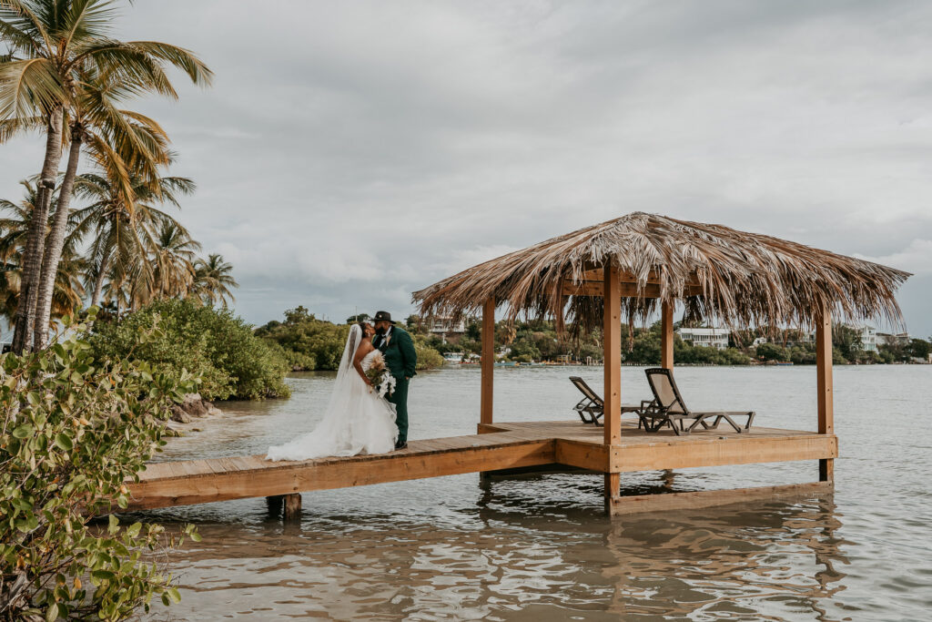Newlywed couple posing next to the wedding gazebo with the beach and Caribbean horizon behind them at Copamarina Beach Resort.