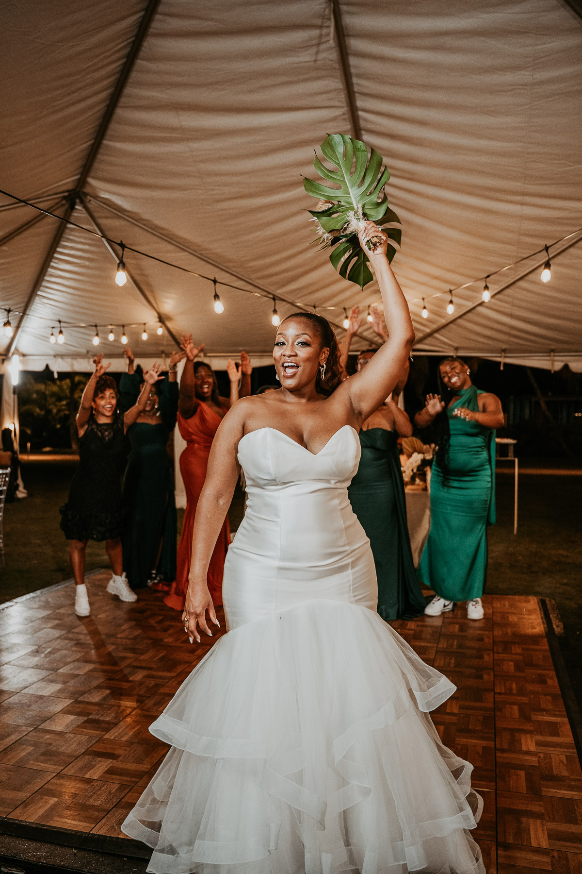 Bride tossing her bouquet as wedding guests reach up to catch it during the reception.