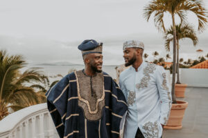 Two grooms standing together on balcony overlooking Fajardo coastline