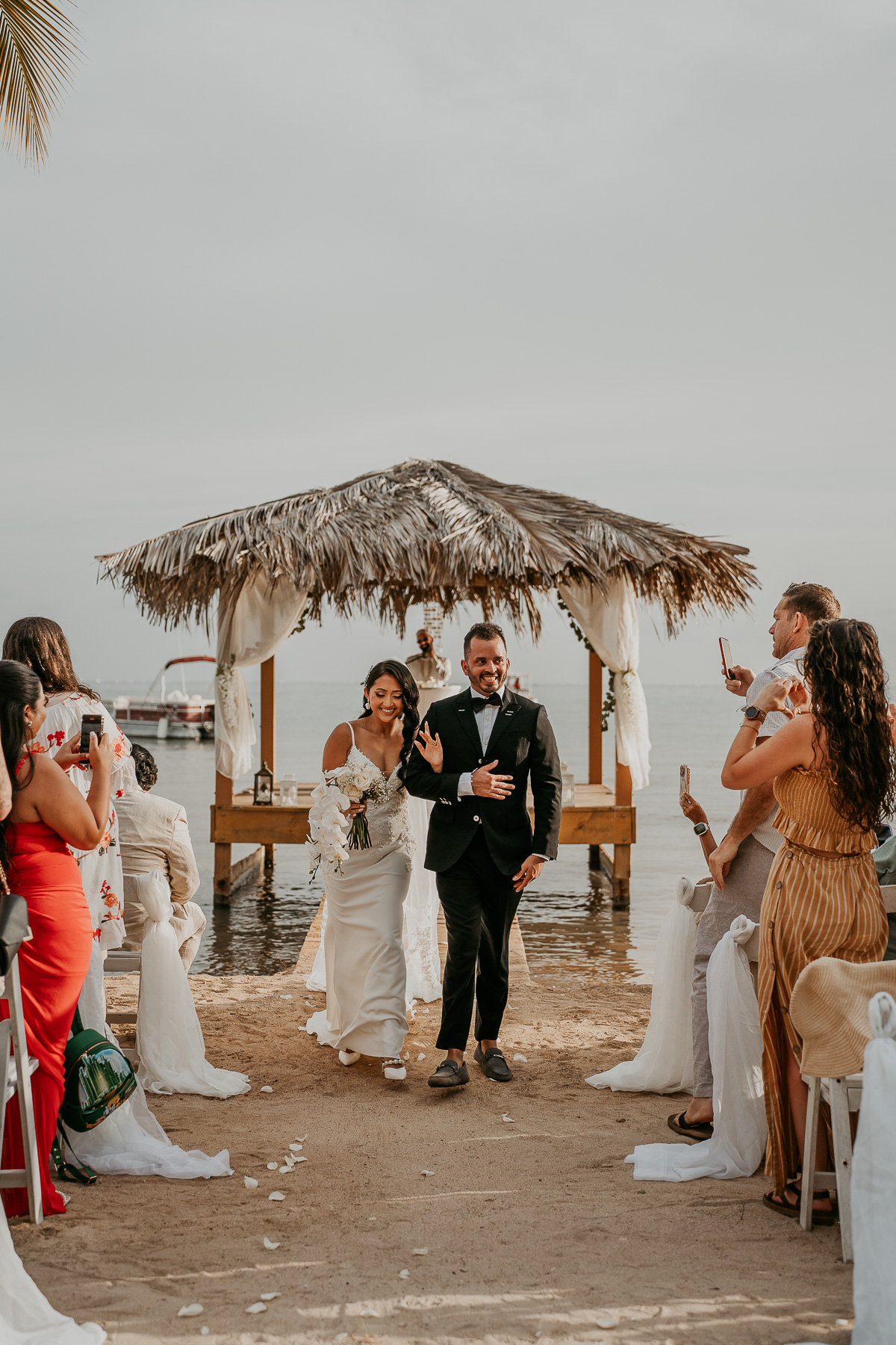 Bride and groom walking hand in hand along the serene beach of Copamarina.