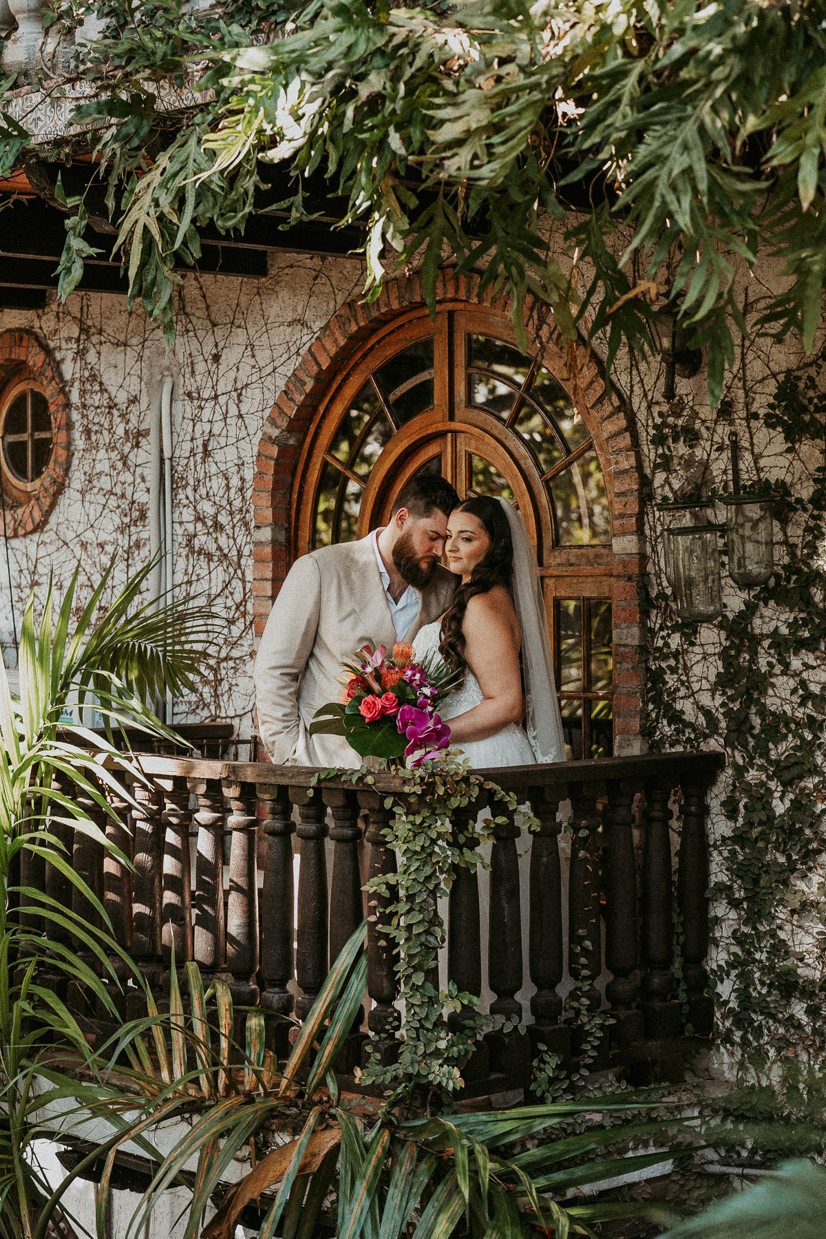 Bride and groom embracing beneath the tropical greenery