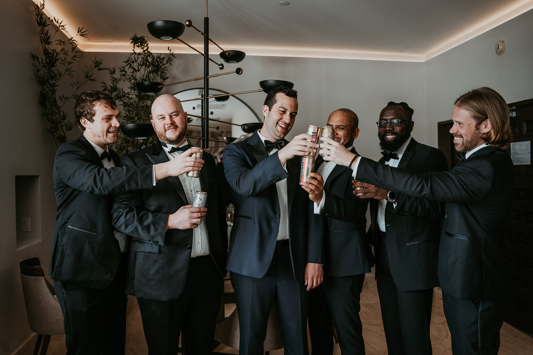 Groomsmen laughing together while raising a toast in the hotel.