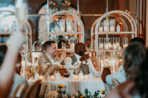 The grooms smile and interact with guests during their wedding toast.