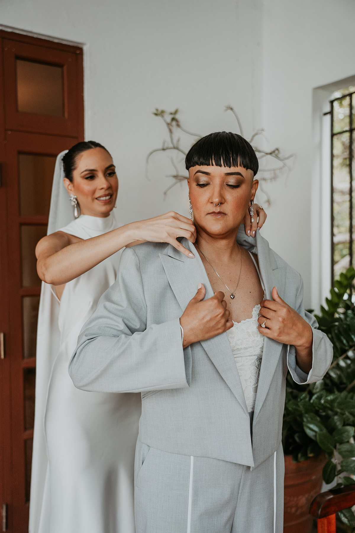 Bride helping her partner adjust her suit while getting ready for their wedding