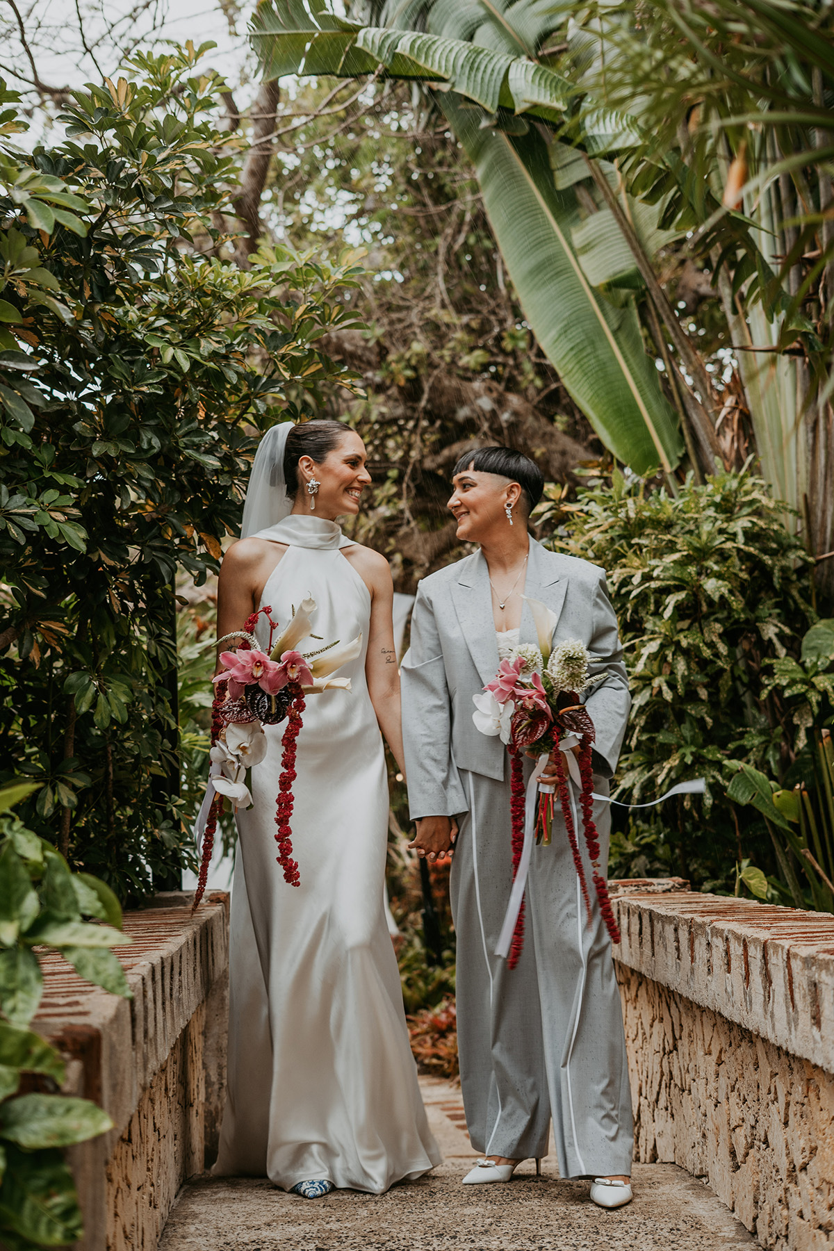 Two brides walking together through the gardens before their wedding ceremony