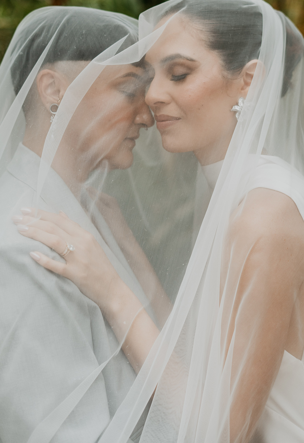 Newlywed lesbian couple embracing under veil