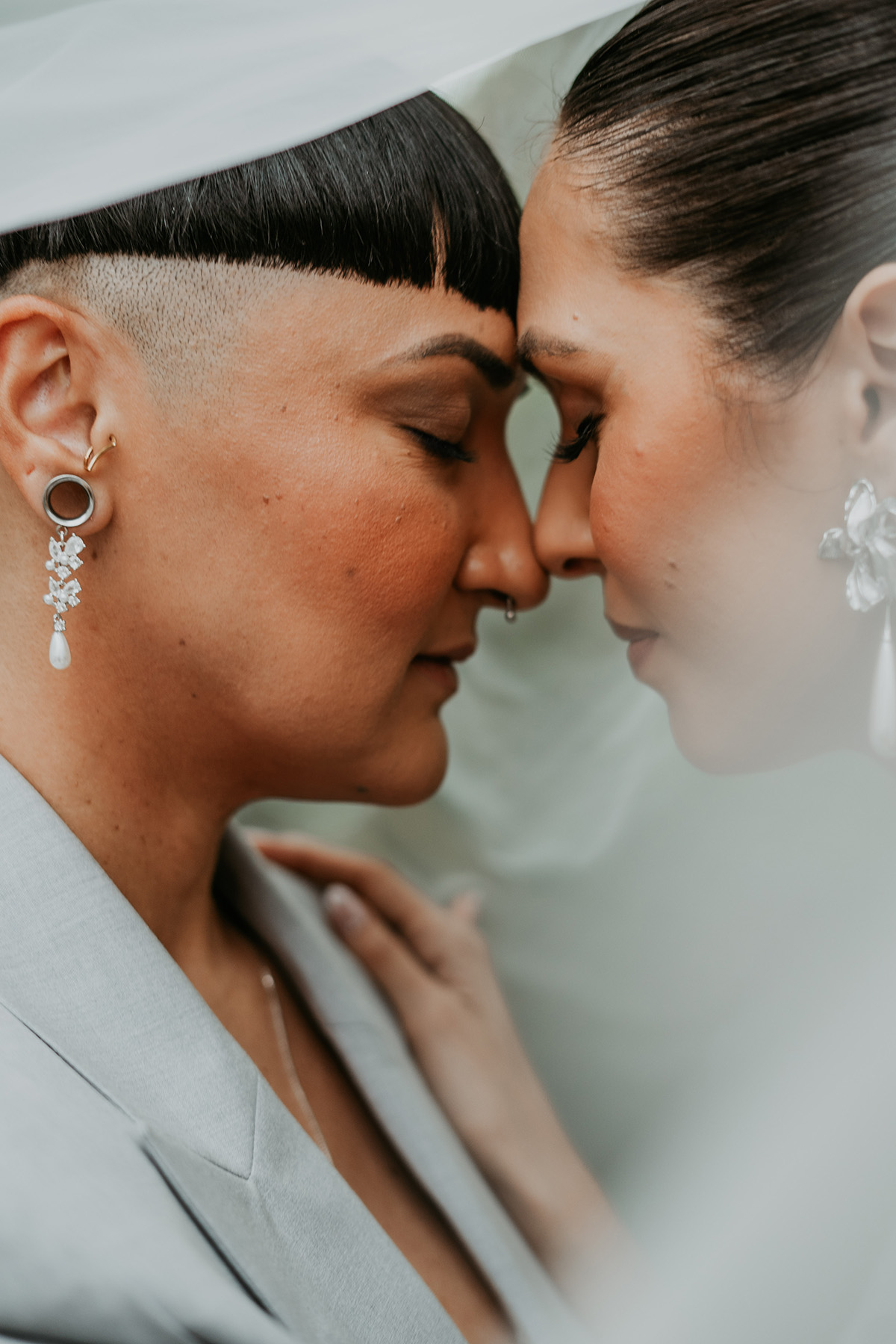Lesbian newlywed couple embracing each other under the veil at their Jardines del Castillo wedding