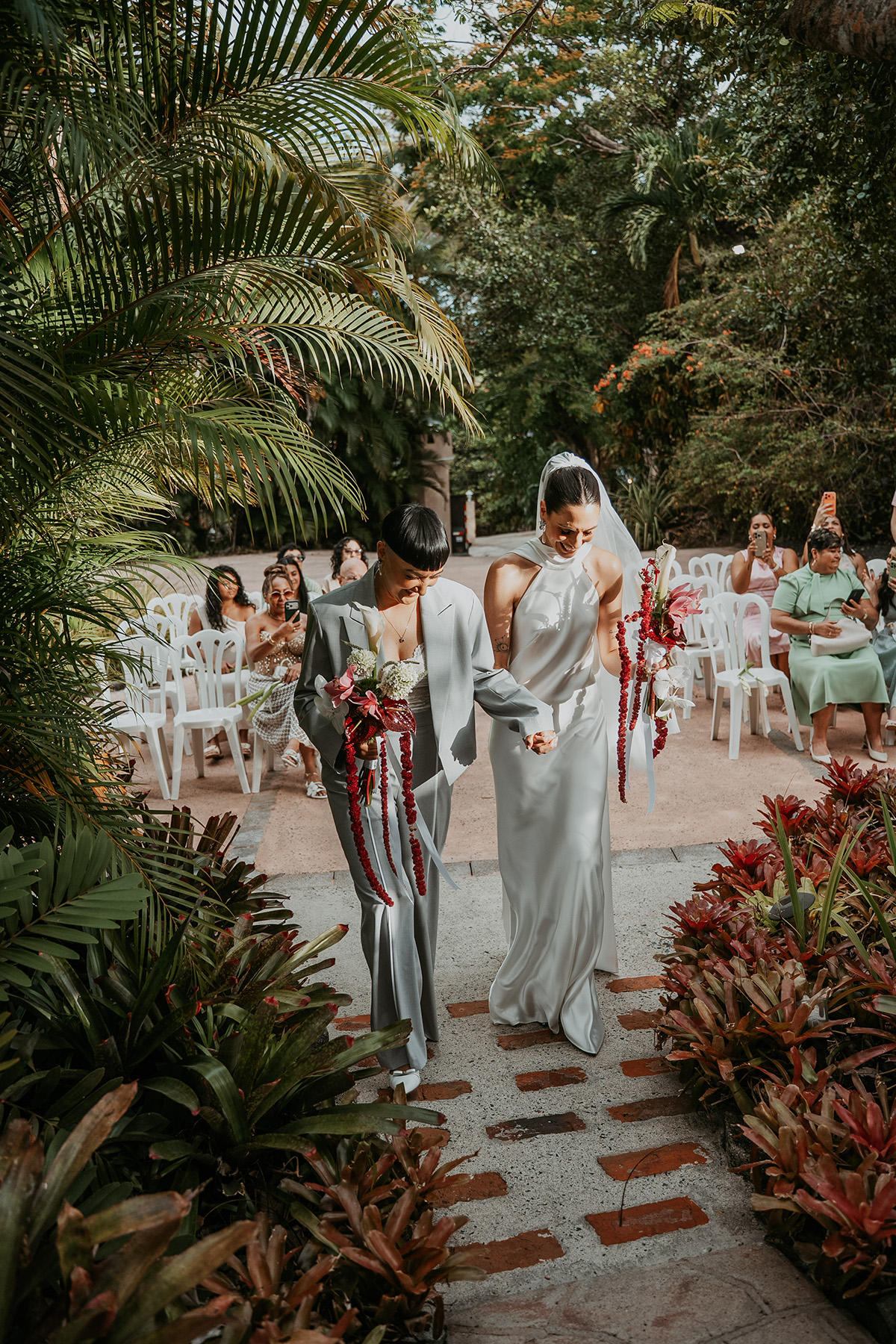 Two brides walking down the aisle together at Jardines del Castillo