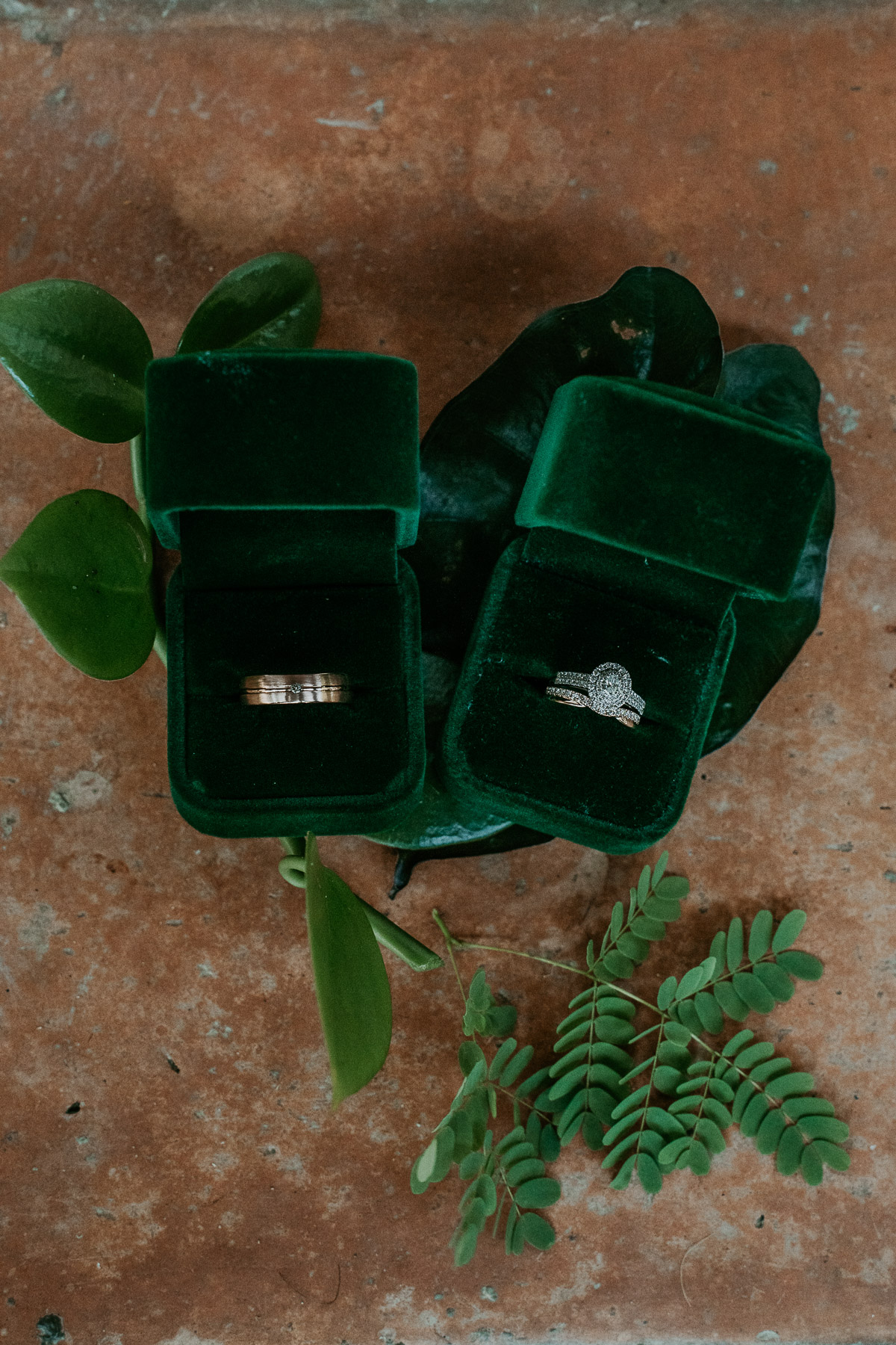 Wedding rings with green velvet boxes and greenery.