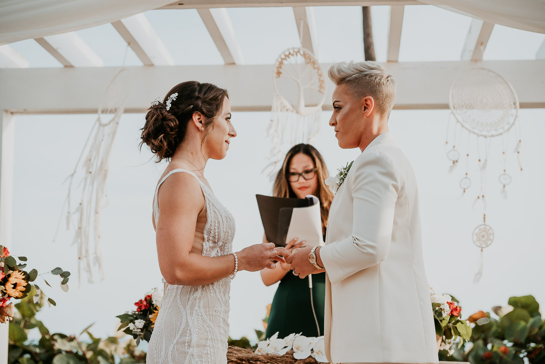 Two brides exchanging vows with the ocean as a backdrop.