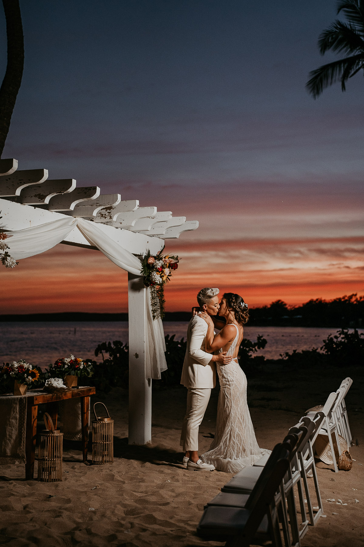 Romantic sunset portrait of two brides kissing on the beach.