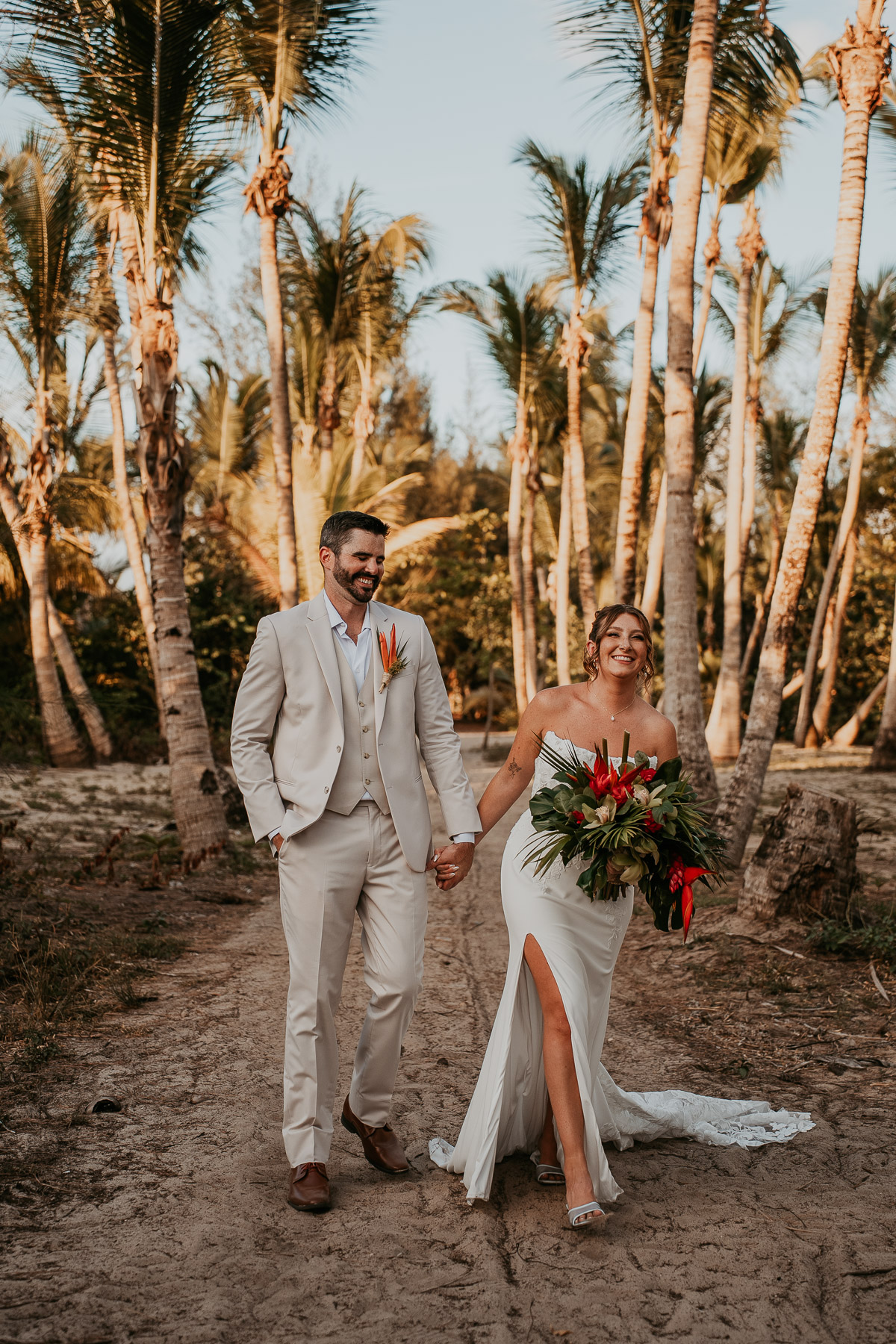 Newly wed couple walking down palm groove at beach in Isla Verde