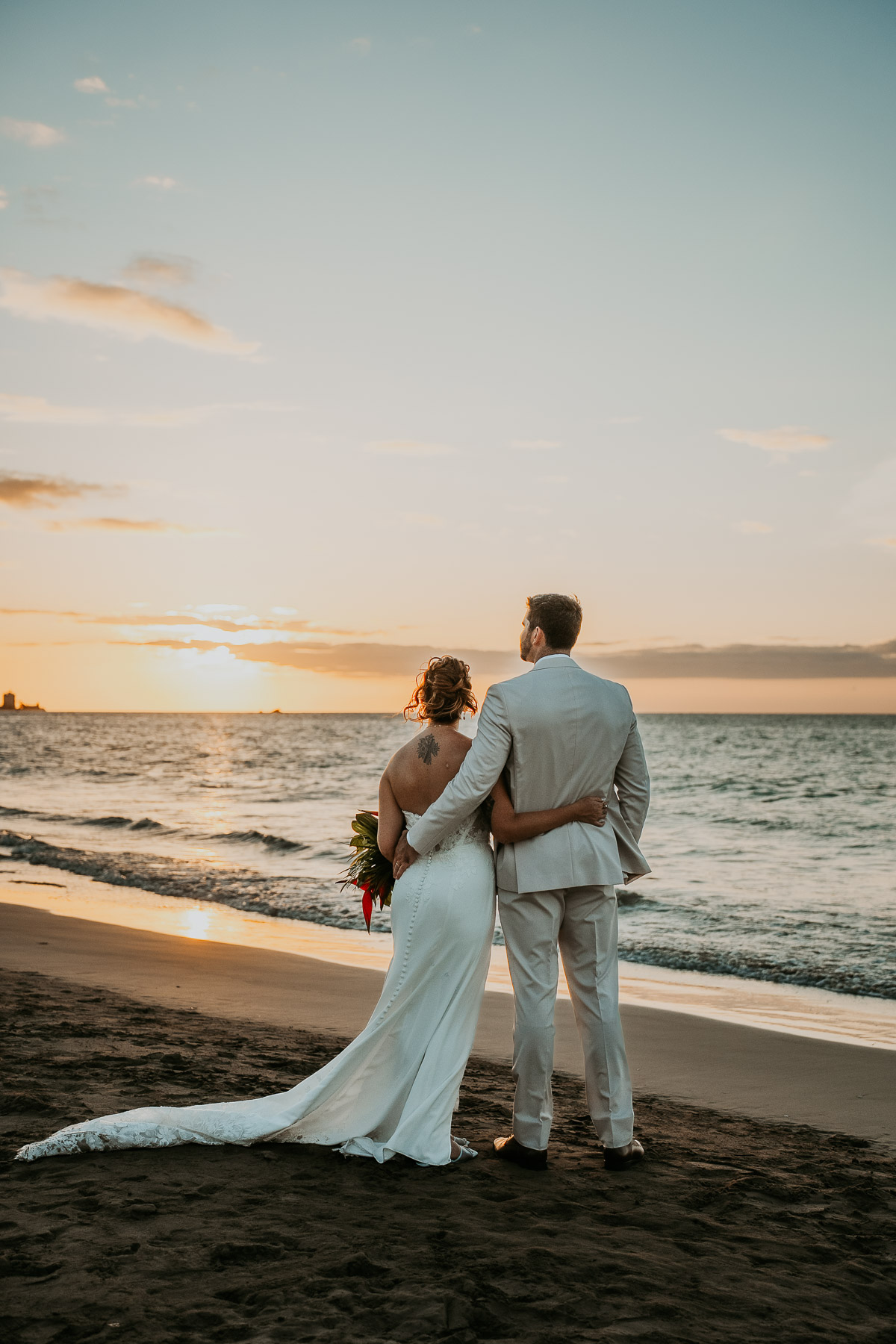 Intimate moment of newlywed couple overlooking the sunset at the ocean