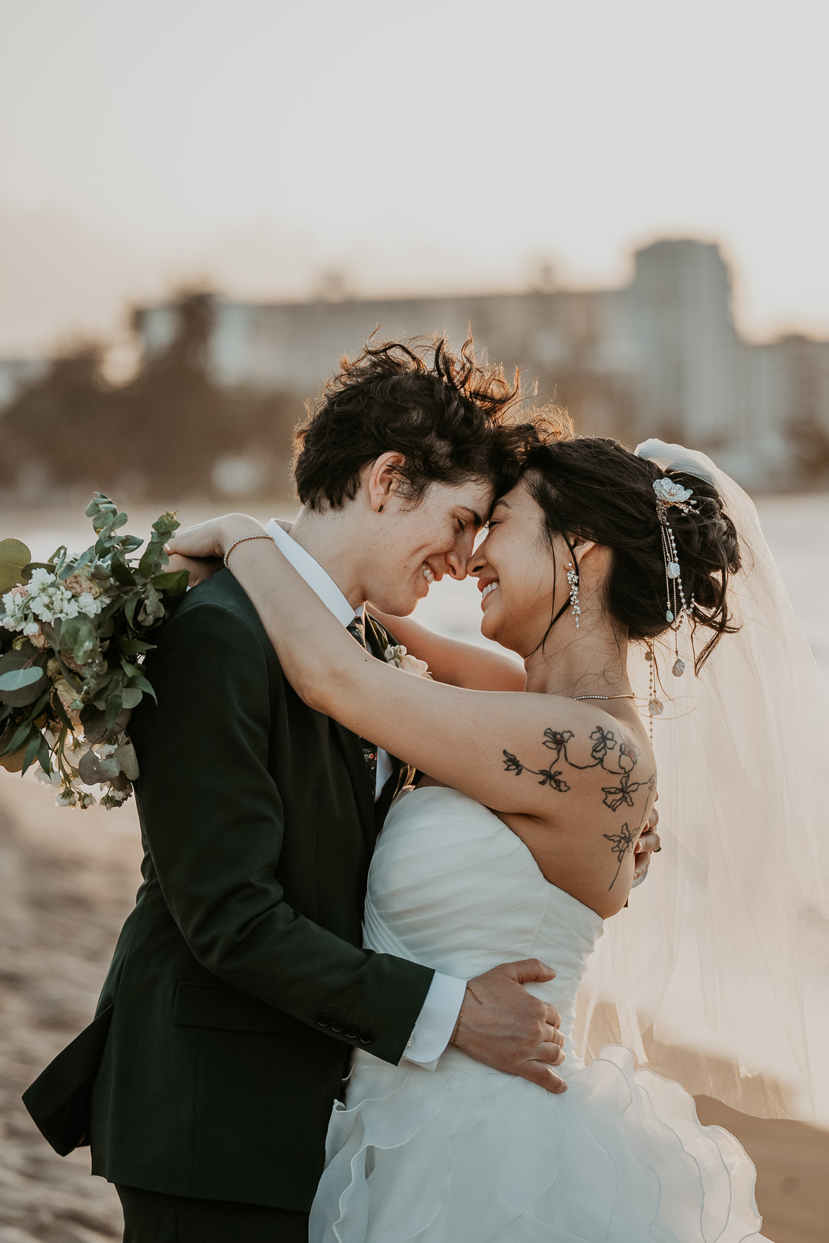 Portrait of a lesbian couple embracing each other on the shore of a coastal hotel wedding location.