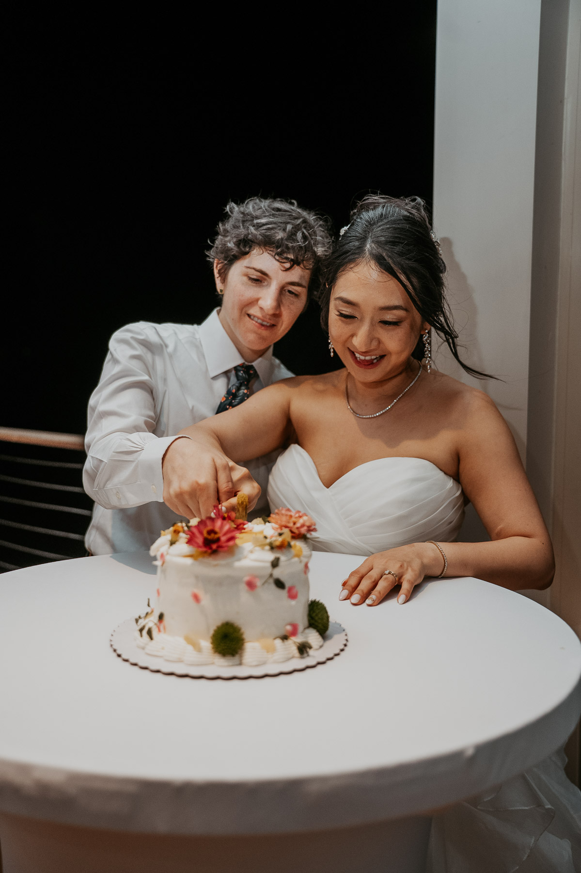 The lesbian couple cutting their wedding cake together during the late night reception.