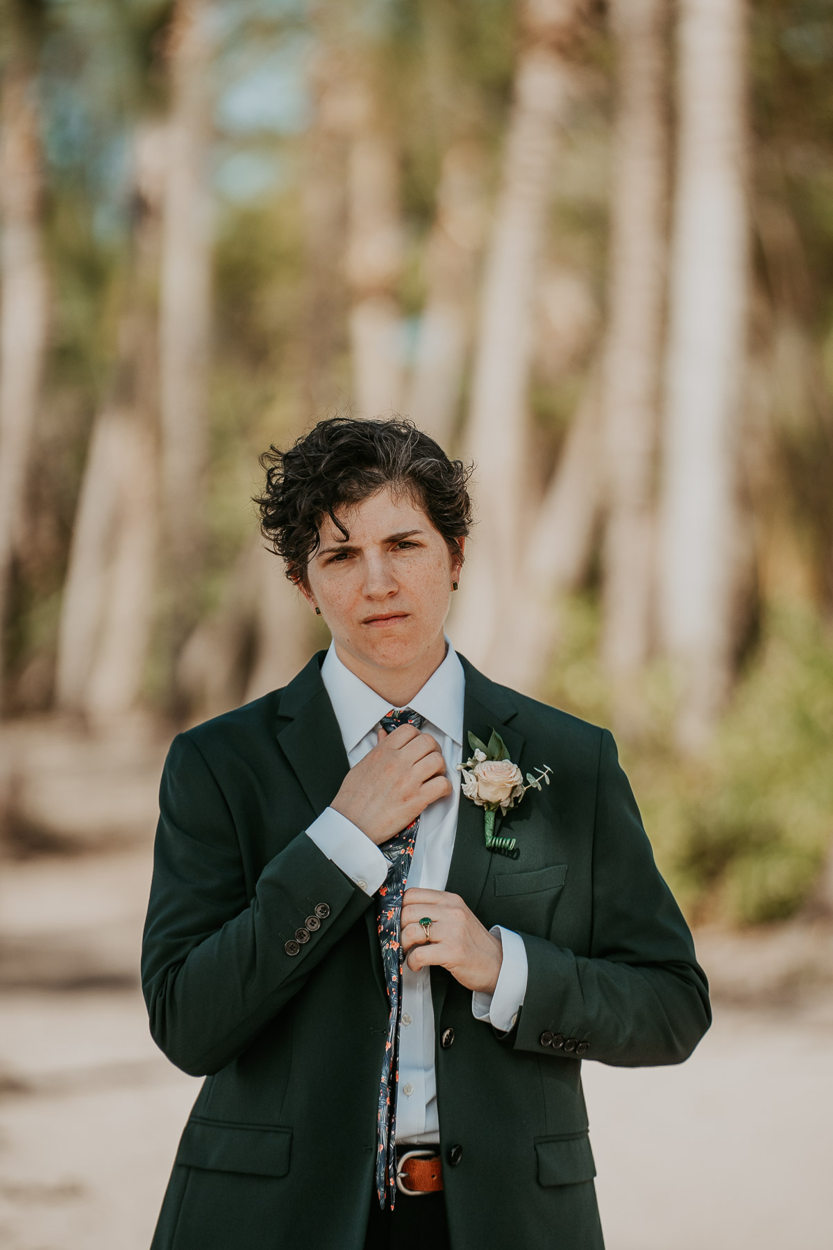 Portrait photo of a masculine-presenting bride adjusting her suit jacket before the ceremony.