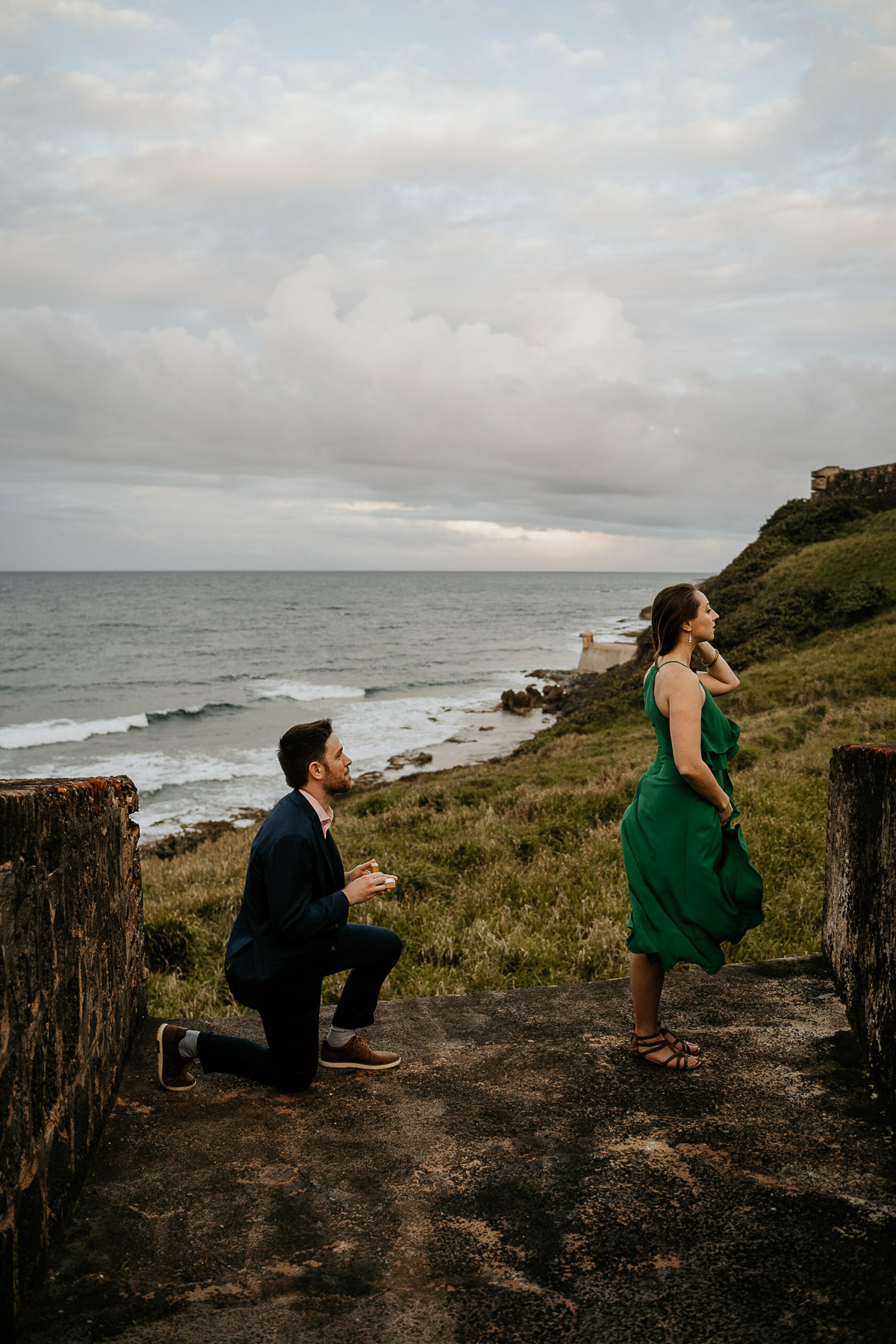 The moment of surprise: a partner down on one knee proposing under the soft, overcast sky in Old San Juan