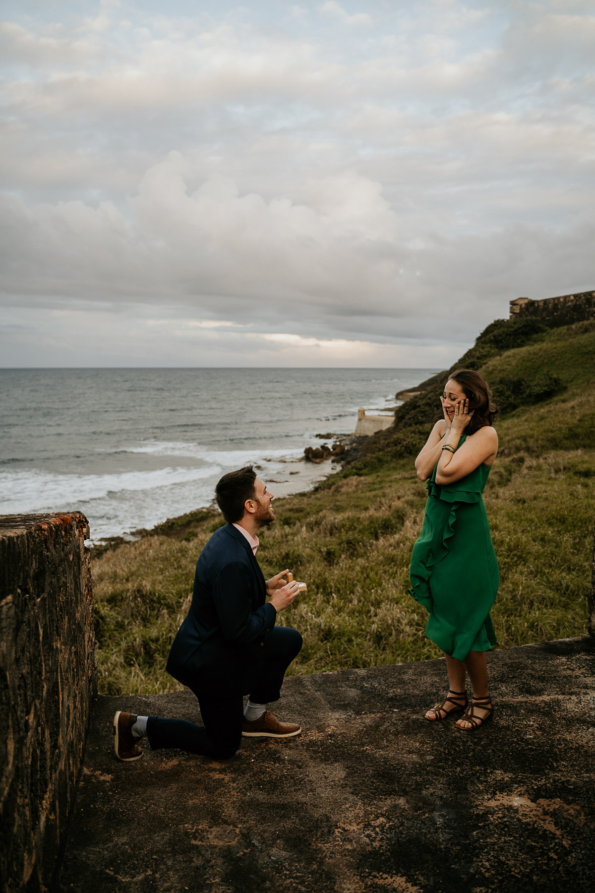 The moment of surprise: a partner down on one knee proposing under the soft, overcast sky in Old San Juan.