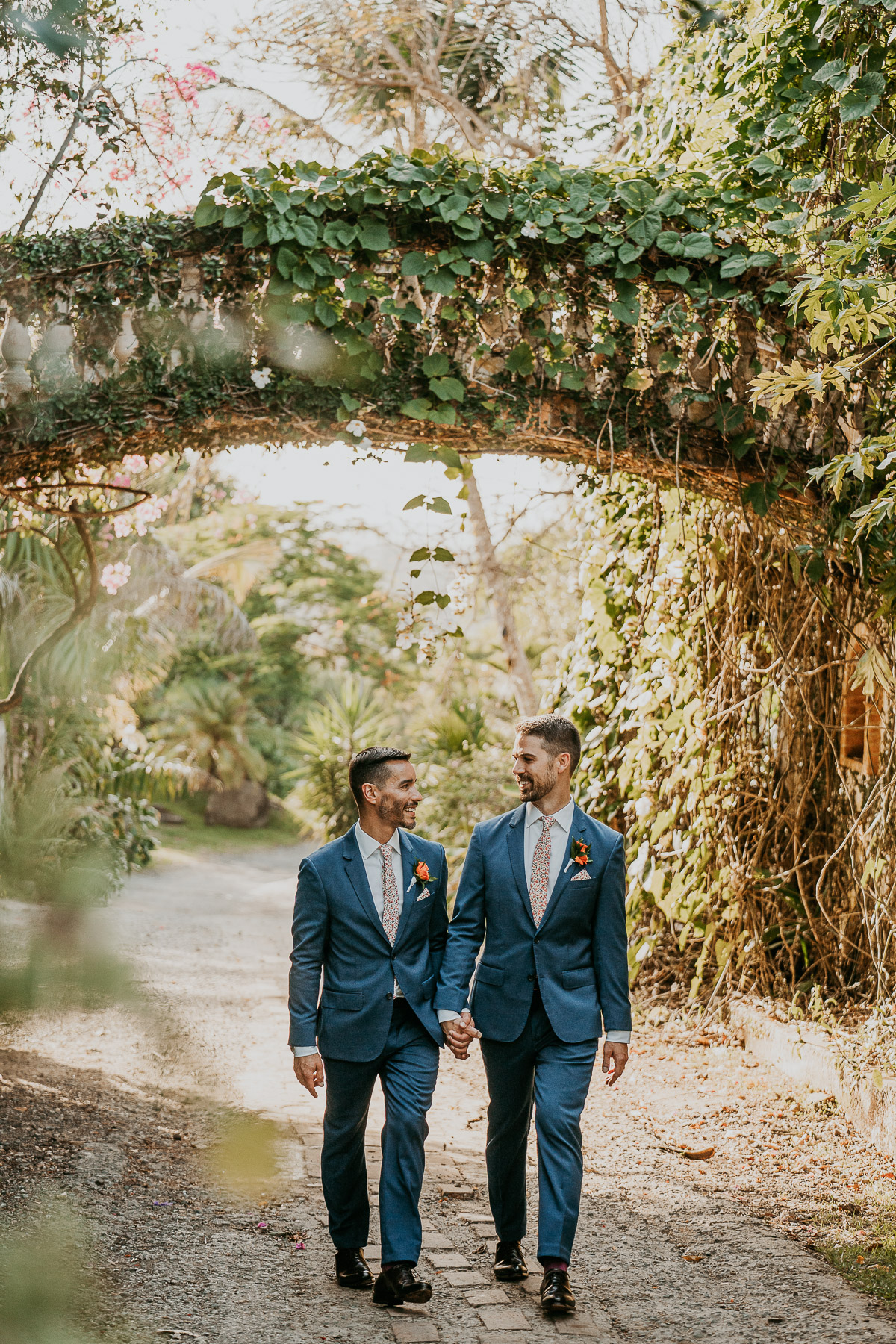 Grooms under archway of Hacienda Siesta Alegre LGBTQ+ wedding