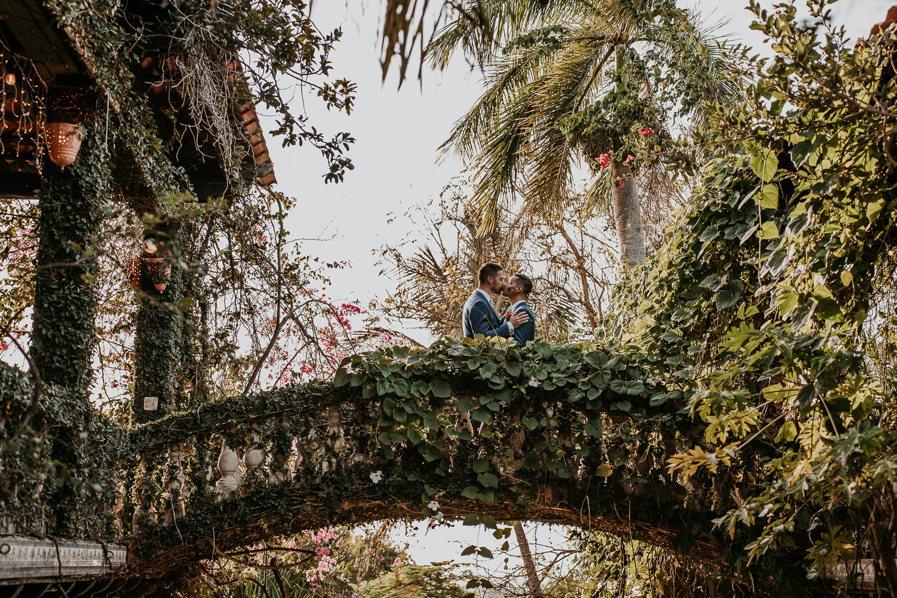 Grooms under archway of Hacienda Siesta Alegre LGBTQ+ wedding