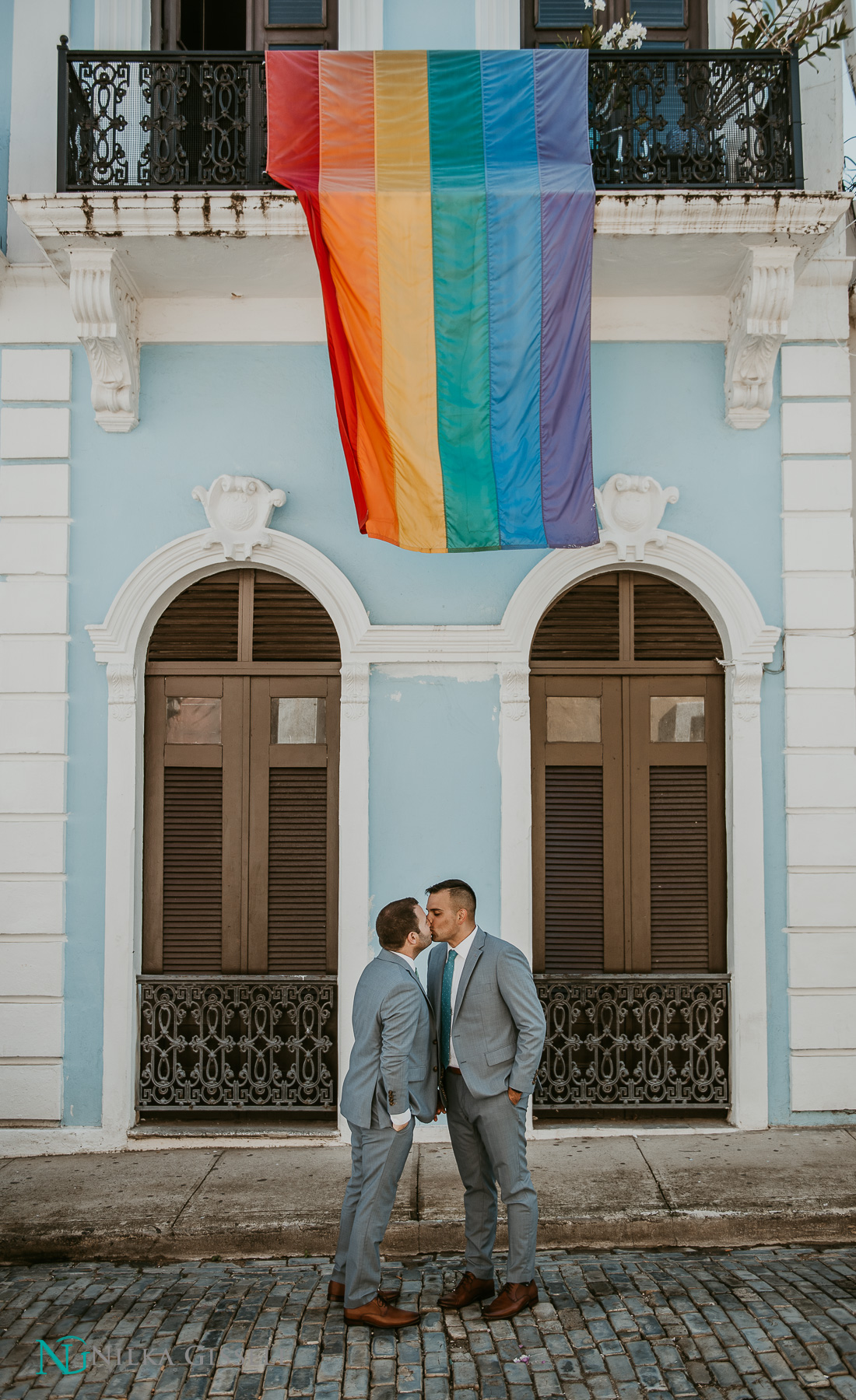 Two grooms kiss underneath a Pride Flag at Old San Juan during their LGBTQ+ wedding