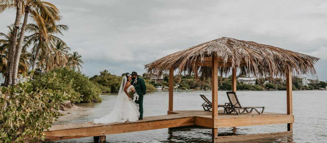Newlywed couple posing next to the wedding gazebo with the beach and Caribbean horizon behind them at Copamarina Beach Resort.