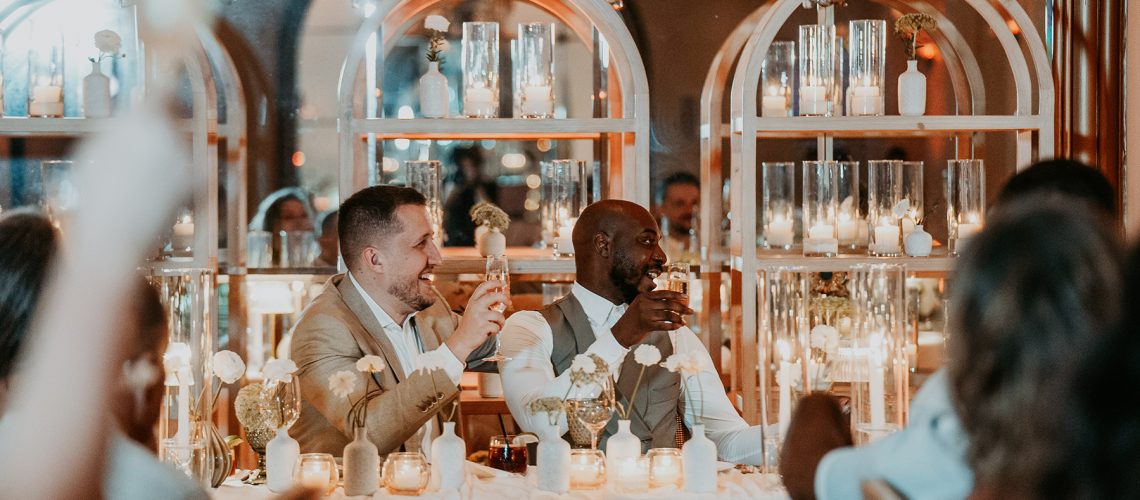 The grooms smile and interact with guests during their wedding toast.