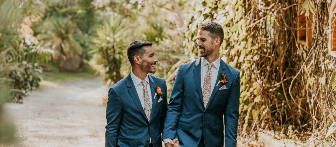 Grooms under archway of Hacienda Siesta Alegre LGBTQ+ wedding