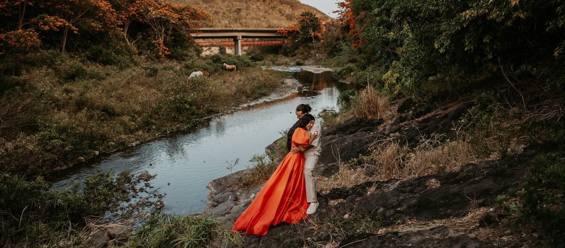 Puerto Rico adventure engagement session with couple embracing beside a river, lush greenery, flamboyán trees and wild horses